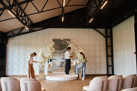 Kreatives Team von Eventdesignern bereitet moderne Festhalle vor, indem es florale Kompositionen arrangiert