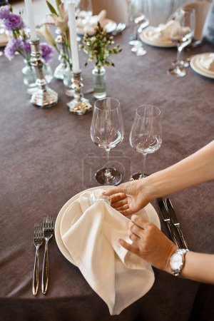 Téléchargez les photos : Vue recadrée du décorateur tenant des serviettes près des assiettes sur la table avec cadre festif, configuration de l'événement - en image libre de droit