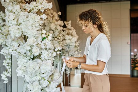 Téléchargez les photos : Fleuriste créatif avec ruban blanc arrangeant décor floral blanc dans la salle de banquet pour une occasion spéciale - en image libre de droit