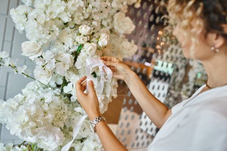 Fleuriste créatif attachant ruban blanc sur la composition florale en fleurs dans la salle des événements, cadre de banquet