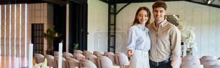 mujer sonriente señalando con el dedo mientras está de pie con el novio en la sala de eventos moderna, pancarta