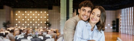 glücklicher Mann umarmt lächelnde Freundin im geschmückten Bankettsaal, Hochzeitsvorbereitung, Banner