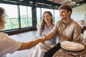 happy man shaking hands with event coordinator near pleased girlfriend in modern wedding venue Poster #675850656