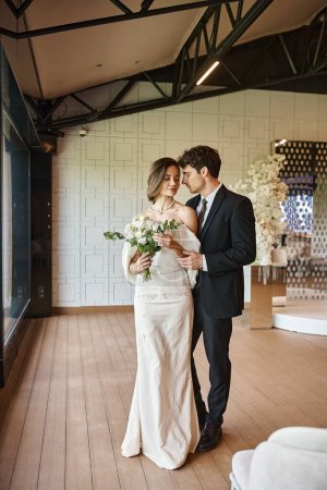 in voller Länge junge elegante Paare in Hochzeitskleidung im modernen Bankettsaal mit floralem Dekor