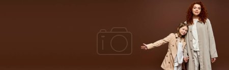 Téléchargez les photos : Génération, mère bouclée tenant la main avec sa fille et debout en manteaux sur fond brun, bannière - en image libre de droit