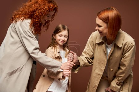 générations, heureuse famille rousse en manteaux empilant les mains ensemble sur fond brun, les femmes et les filles