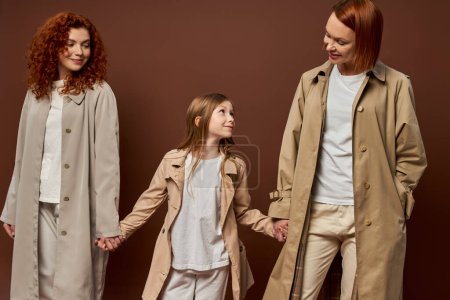 trois générations, joyeuse famille rousse en manteaux tenant la main sur fond brun, les femmes et les filles