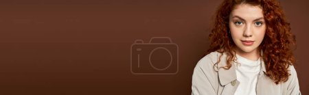 Photo for Portrait of redhead woman with curly hair looking at camera on brown background, autumn banner - Royalty Free Image