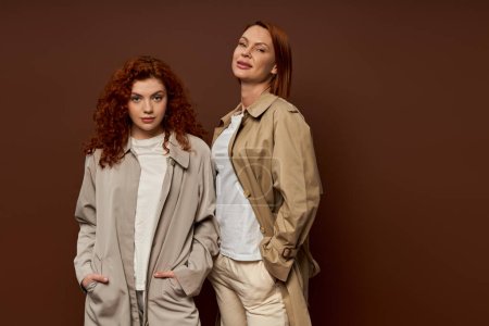 deux générations, femmes rousses en tenue d'automne tendance posant sur fond brun, trench coats