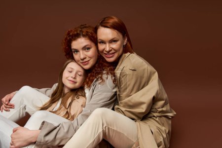 drei Generationen von Frauen, positive rothaarige Familie blickt in die Kamera auf braunem Hintergrund, Herbst