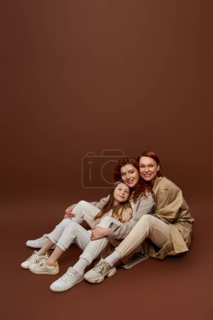 three generations, positive redhead family looking at camera on brown background, women and child