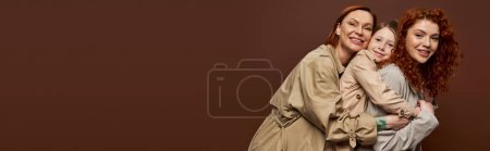 happy redhead family of three female generations hugging on brown background, autumn fashion, banner