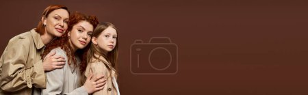 Téléchargez les photos : Famille de trois générations féminines aux cheveux roux posant en manteaux beiges sur fond marron, bannière - en image libre de droit
