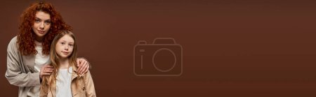 Téléchargez les photos : Générations, mère bouclée aux cheveux roux regardant caméra avec fille sur fond brun, bannière - en image libre de droit