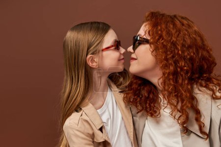 two generations, happy redhead mother and daughter in sunglasses on brown backdrop, face to face