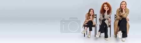 Photo for Female generations, happy redhead women and child sitting in row on chairs on grey backdrop - Royalty Free Image