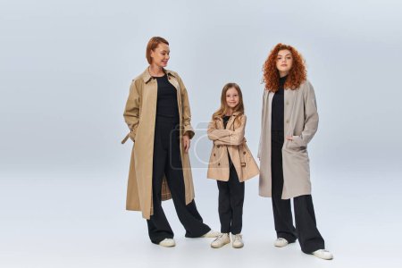 redhead family in coats posing and standing together on grey background, happy female generations