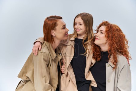 cute redhead girl hugging happy women in autumn coats on grey background, female generations