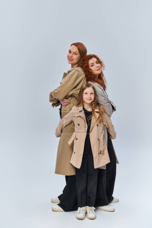 rousse fille câlin heureux parents dans des manteaux sur fond gris, les générations féminines, pleine longueur