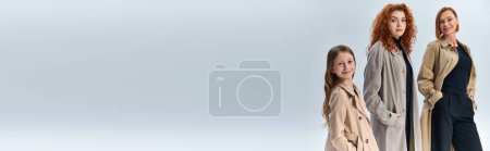Téléchargez les photos : Famille rousse dans des manteaux élégants posant avec les mains dans les poches sur gris, trois générations, bannière - en image libre de droit