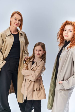 three generation joyful family standing together in autumn coats on grey backdrop, fall fashion