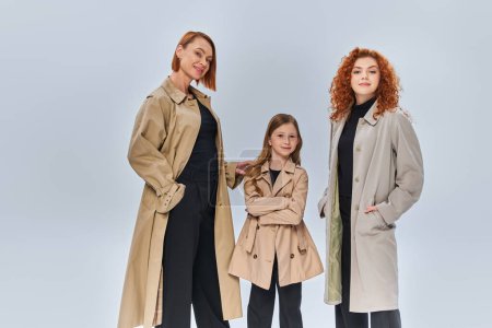 famille de rousses de trois générations posant ensemble en manteaux d'automne sur fond gris, à la mode automne