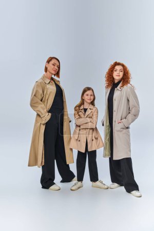 three generation redhead family posing together in autumn coats on grey backdrop, full length