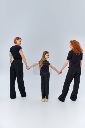 trois générations, heureux rousse famille tenant la main et debout en tenue assortie sur gris