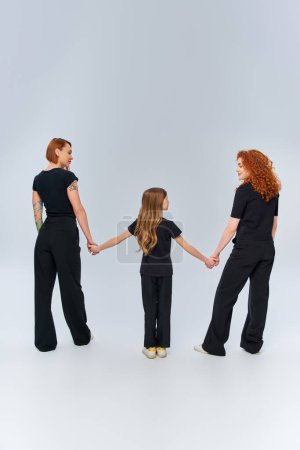 weibliche Generationen, glückliche rothaarige Familie Händchen haltend und in passender Kleidung auf grau