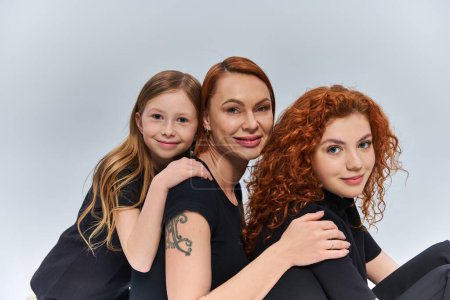 three generations concept, happy redhead family smiling and looking at camera on grey backdrop