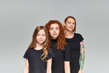 portrait of women red hair posing with girl in matching outfits on grey backdrop, three generations