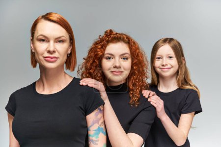 Photo for Three generations of cheerful women and girl posing in matching outfits on grey backdrop, family - Royalty Free Image
