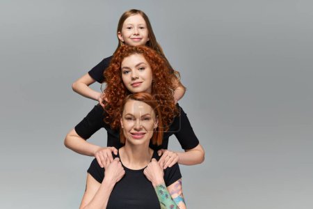 female generations concept, happy redhead family in matching attire hugging on grey background