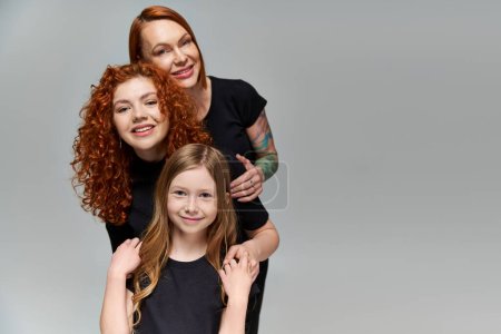 Generationen Konzept, entzückende Familie mit roten Haaren posiert in passender Kleidung auf grauem Hintergrund