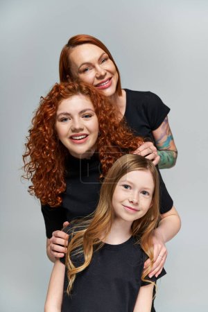 Generationenkonzept, fröhliche Familie mit roten Haaren posiert in passenden Outfits auf grauem Hintergrund