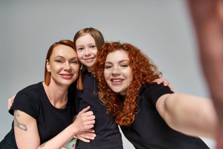 Konzept weiblicher Generationen, rothaarige Frauen machen Selfie mit sommersprossigen Mädchen auf grauem Hintergrund