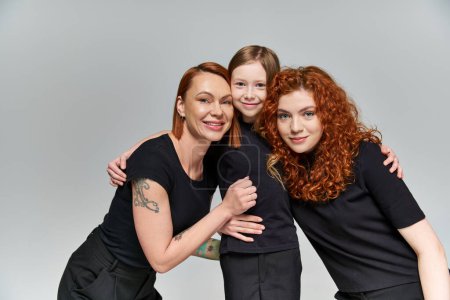 Familienporträt, glückliches sommersprossiges Mädchen umarmt rothaarige Familie in passender Kleidung auf grauem Hintergrund