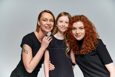 family portrait, freckled girl smiling near redhead family in matching attire on grey background
