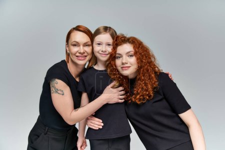 family portrait, redhead women and freckled girl in matching attire smiling on grey background