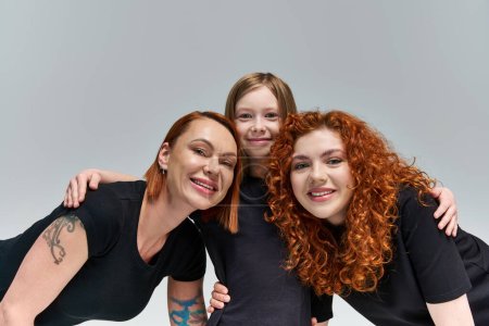 family portrait, happy freckled girl hugging redhead women in matching attire  on grey background