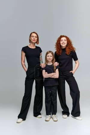 retrato familiar, tres generaciones de mujeres en ropa a juego de pie sobre fondo gris