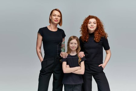 tres generaciones de mujeres en ropa a juego de pie sobre fondo gris, familia con estilo