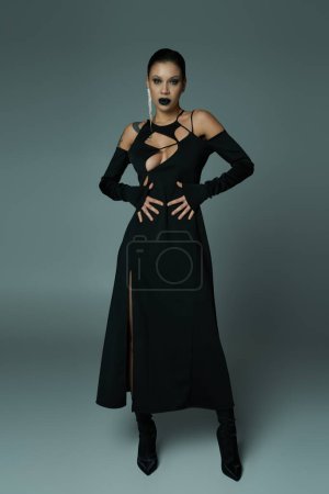 Téléchargez les photos : Femme envoûtante en robe noire enchanteresse et maquillage sur gris, concept halloween - en image libre de droit