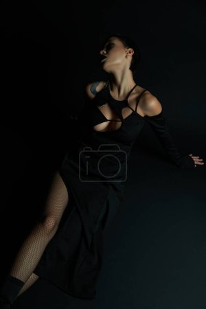 apasionada mujer tatuada en vestido de halloween sexy sentado sobre fondo negro, belleza gótica