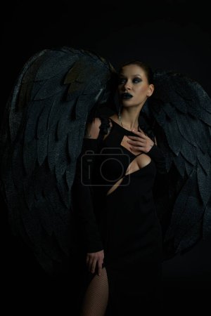 Tätowierte Frau im Halloween-Kostüm gefallener Engel mit Flügeln, die vom schwarzen, dämonischen Charme wegschauen