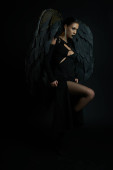 seductive woman in dark makeup and costume with demonic wings looking away on black, Halloween puzzle #676127456