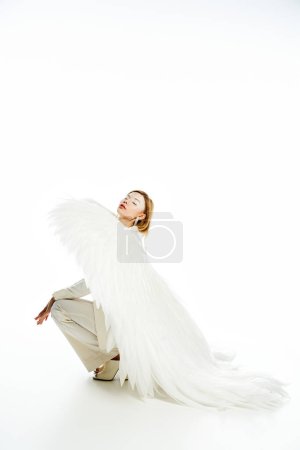 woman in costume of light angel with divine wings sitting on haunches with closed eyes on white
