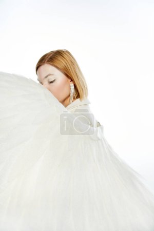 Téléchargez les photos : Femme avec aura angélique visage obscurcissant avec ailes divines sur fond blanc, pureté et sérénité - en image libre de droit