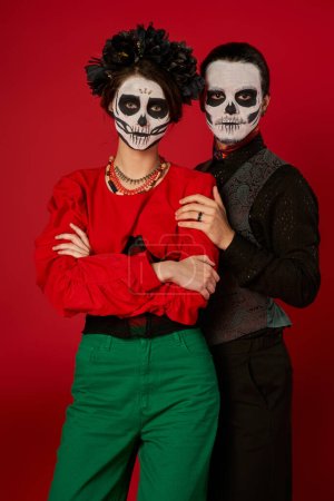 dia de los muertos couple in spooky makeup, man embracing woman with folded arms on red, banner
