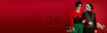 Téléchargez les photos : Couple élégant dans le maquillage catrina posant près de fleurs sur le rouge, dia de los muertos festival, bannière - en image libre de droit